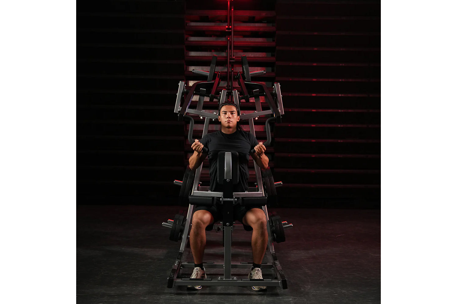 Man using black and red plate-loaded lat pulldown machine in gym setting with red lighting backdrop