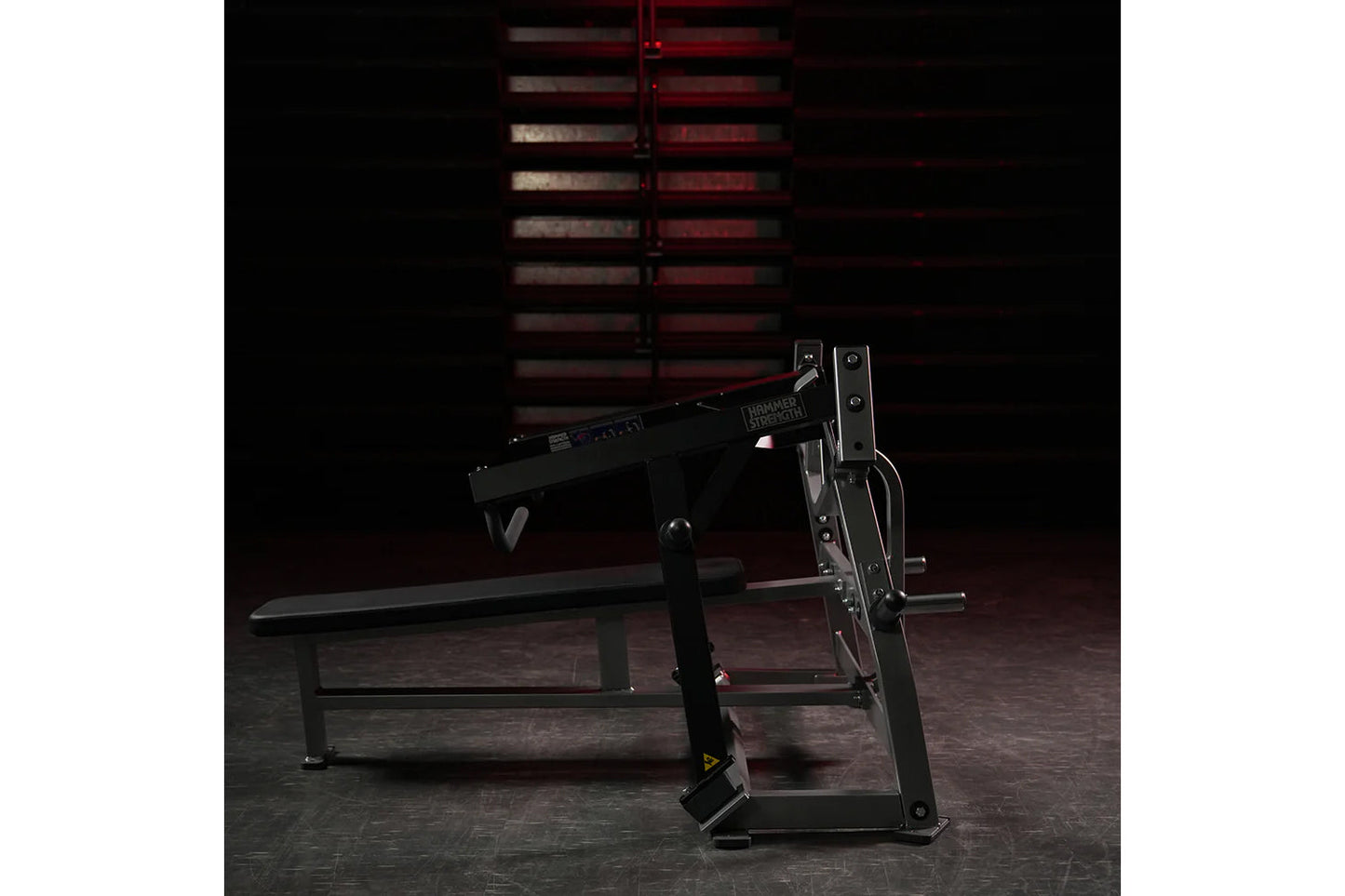 Black plate-loaded iso-lateral horizontal bench press with dual independent weight arms, shown in gym setting with red equipm
