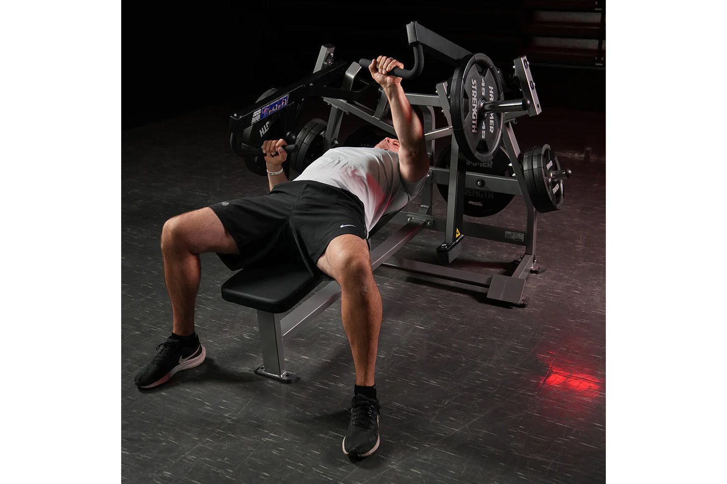 Man performing chest press on black Hammer Strength plate-loaded bench press machine in gym setting