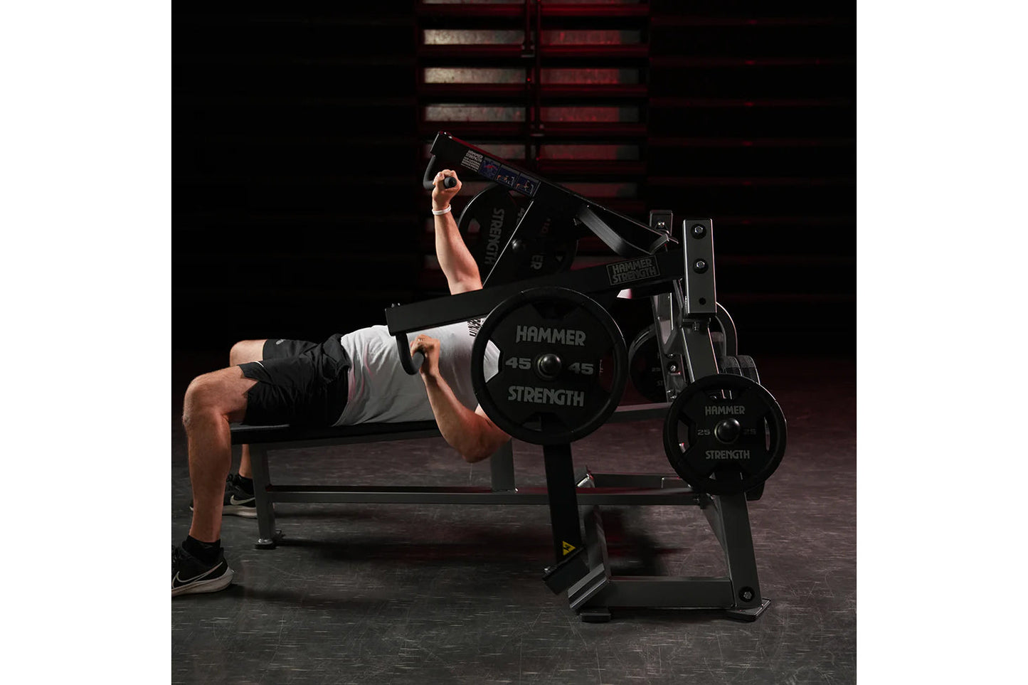 Man performing chest press on black Hammer Strength plate-loaded bench with weight plates, in gym setting
