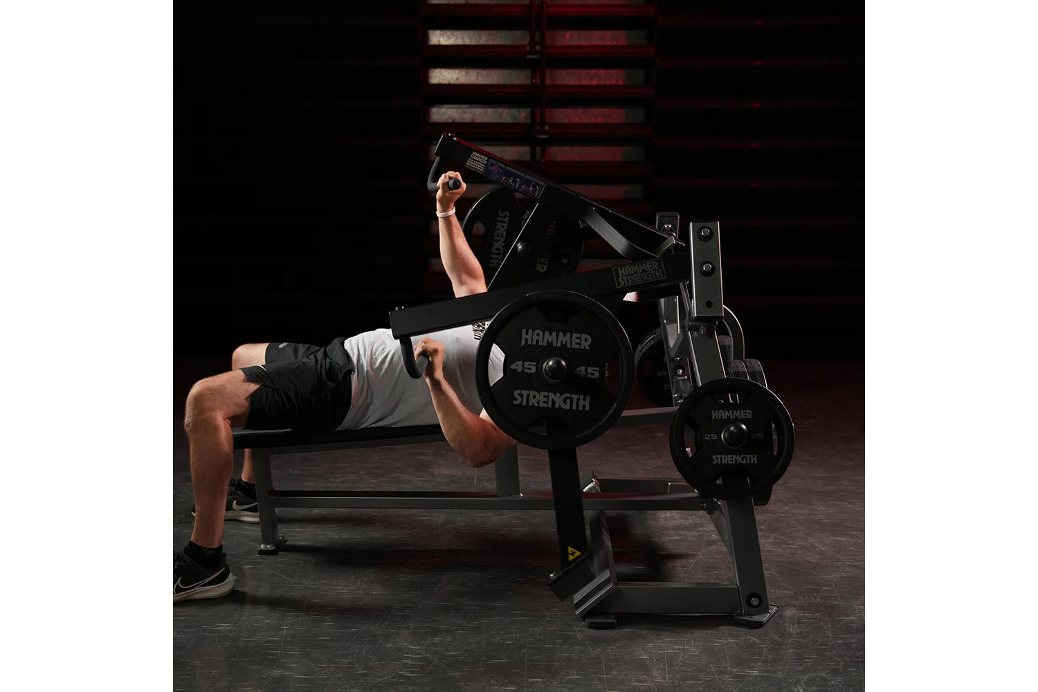 Man performing chest press on black Hammer Strength plate-loaded bench with weight plates, in gym setting