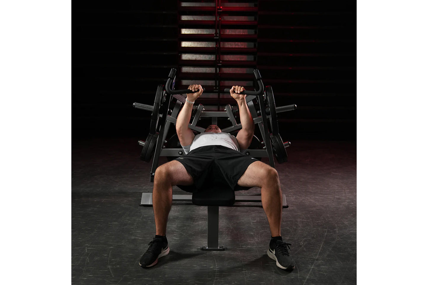 Man performing chest press exercise on black Hammer Strength plate-loaded bench with dumbbells in gym setting