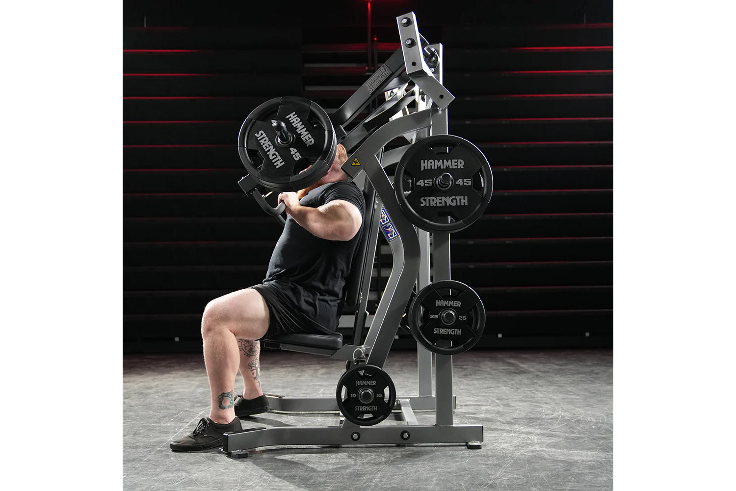 Man performing incline chest press on Hammer Strength plate-loaded machine with black weight plates in gym setting