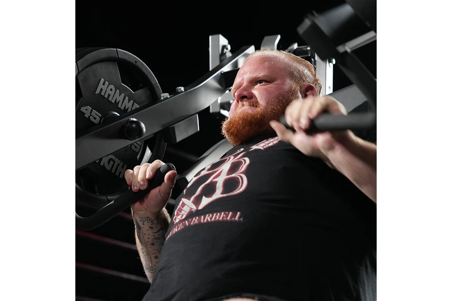 Man wearing black graphic t-shirt using Hammer Strength plate-loaded incline press machine with weighted plates loaded on bot