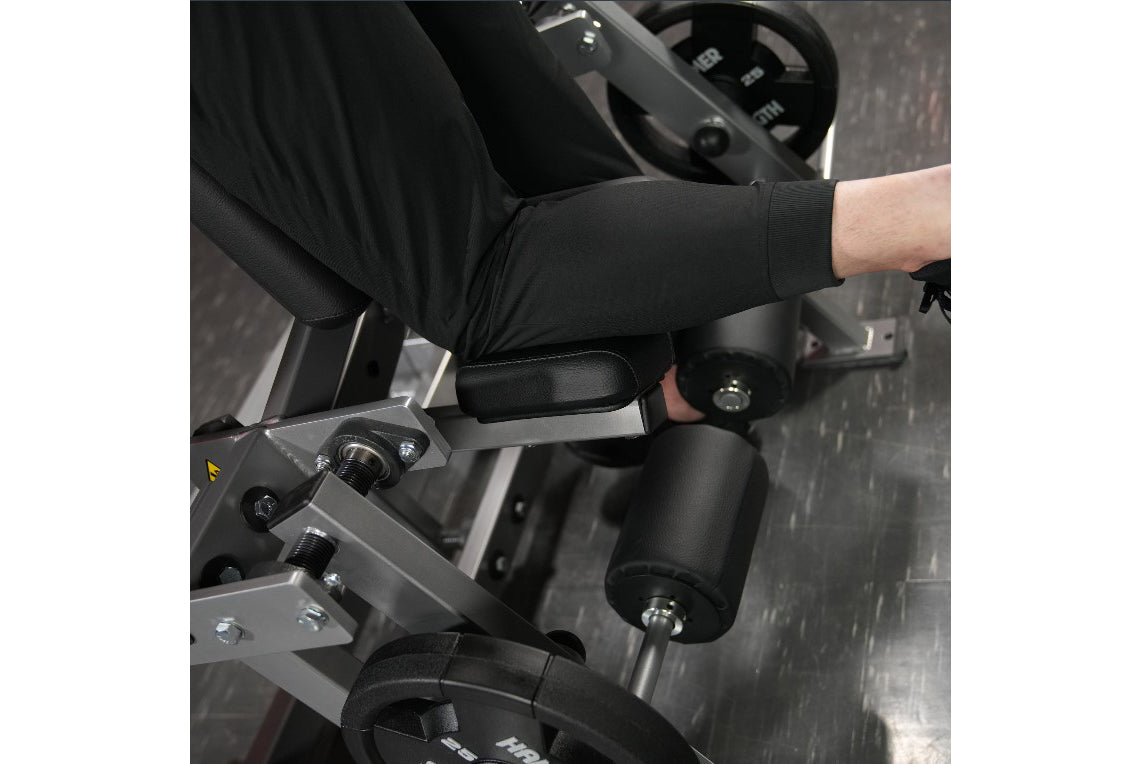 Person using black and gray plate-loaded leg curl machine with padded arm rests and adjustable seat, viewed from above