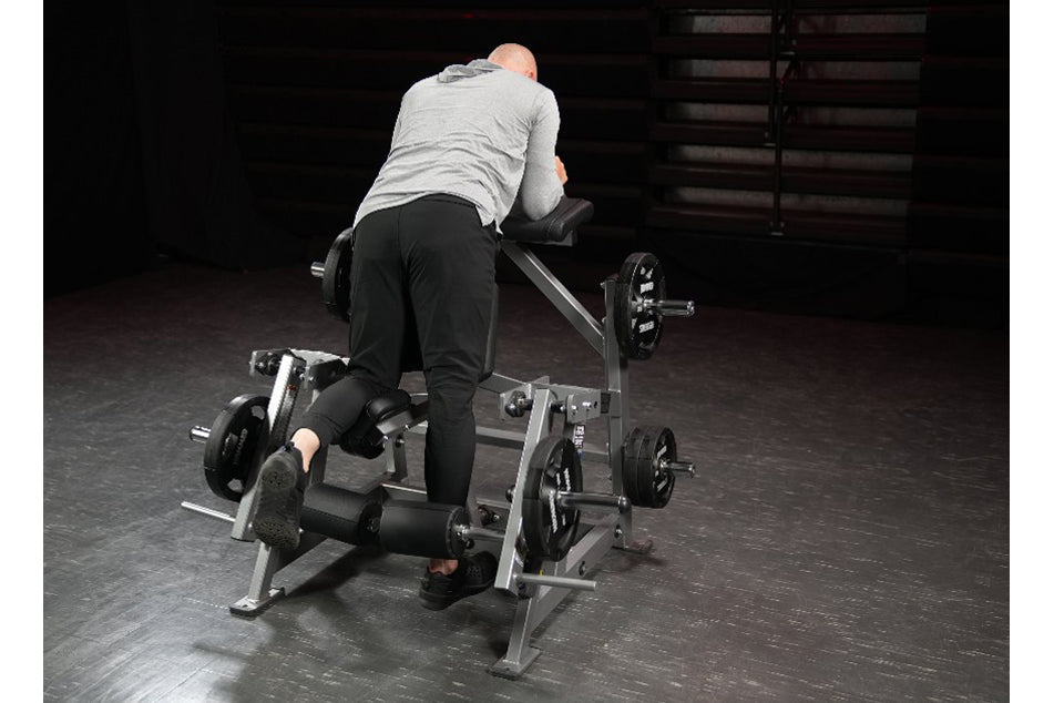 Man using gray and black plate-loaded leg curl machine in gym setting, demonstrating kneeling position