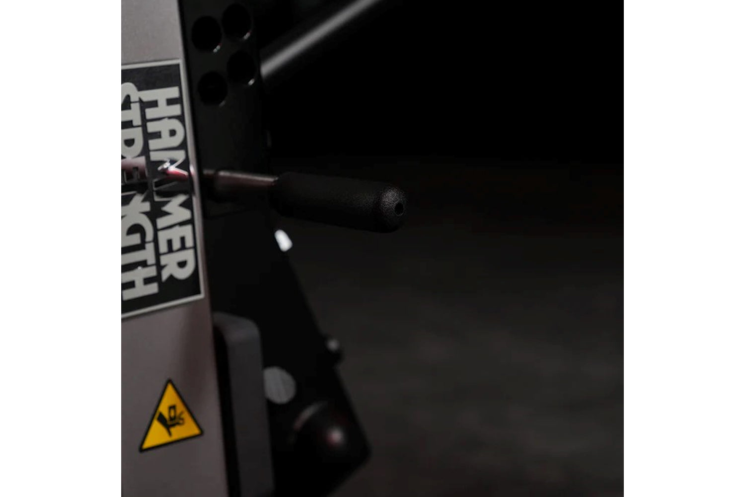 Black Hammer Strength plate-loaded leg curl machine with yellow hazard warning symbol on side panel, detail view