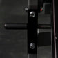Close-up of black plate-loaded leg curl machine with foam handle, metal bolts, and red adjustment knob on dark background