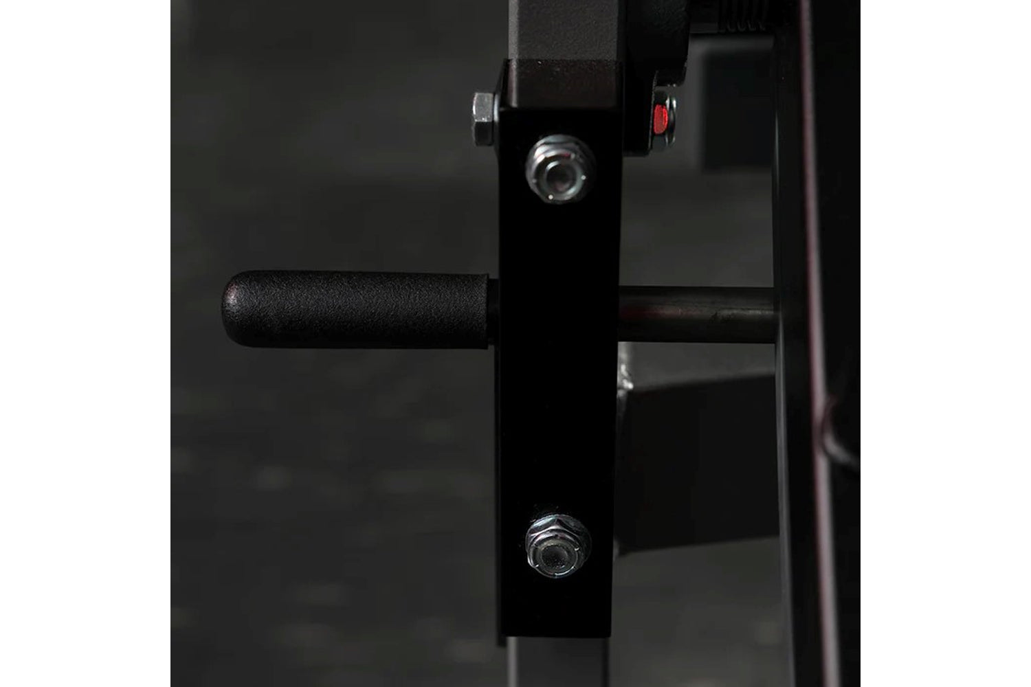 Close-up of black plate-loaded leg curl machine with foam handle, metal bolts, and red adjustment knob on dark background