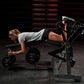 Woman using black Hammer Strength leg curl machine with weighted plates, wearing gray shirt and black shorts in gym setting