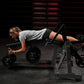 Woman using black plate-loaded leg curl machine with adjustable foot platform and weight plates, wearing gray t-shirt and bla