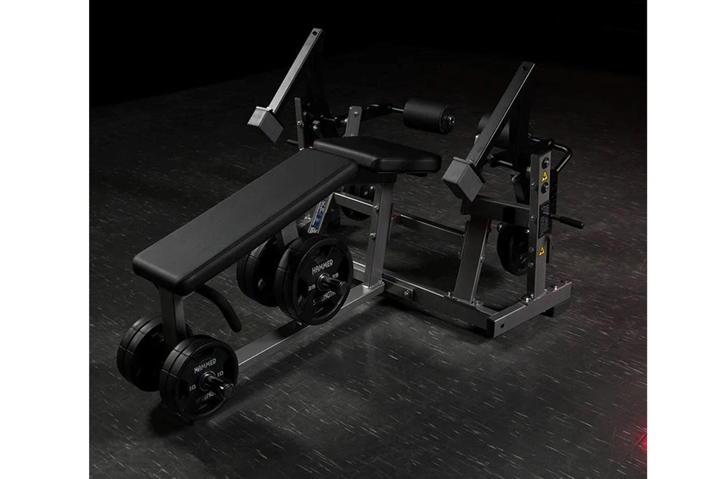Black Hammer Strength plate-loaded leg curl machine with padded seat, weight plates, and dual lever arms on dark gym floor