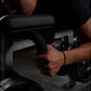 Person gripping black padded handle of plate-loaded leg curl machine during exercise