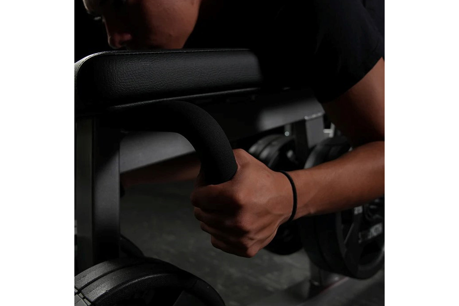 Person gripping black padded handle of plate-loaded leg curl machine during exercise