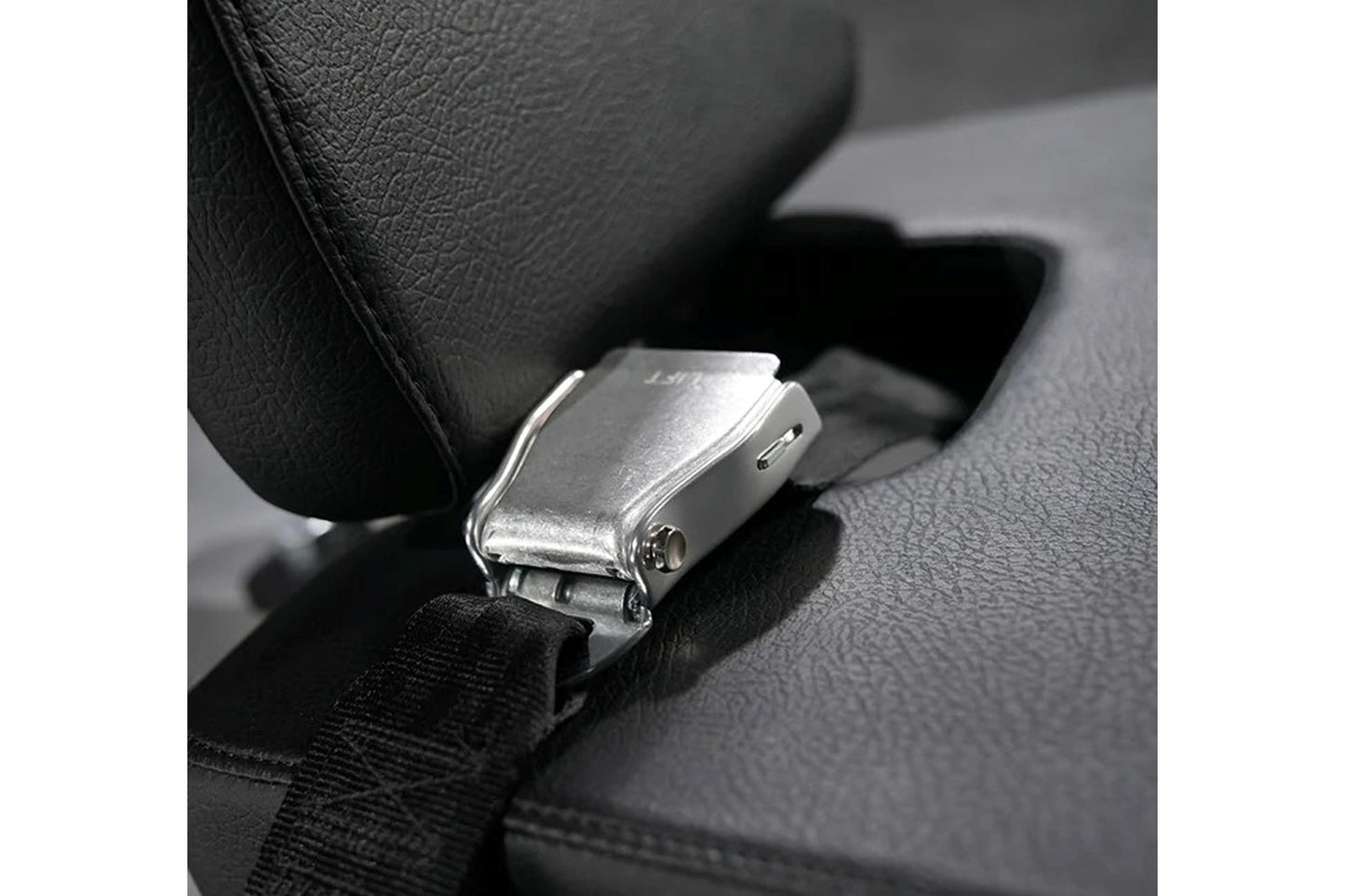 Silver metal seat belt buckle with black fabric strap on dark textured car seat interior