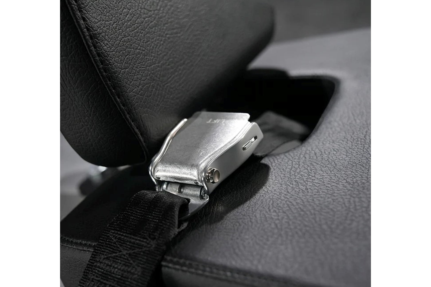 Silver metal seat belt buckle with black fabric strap on dark textured car seat interior
