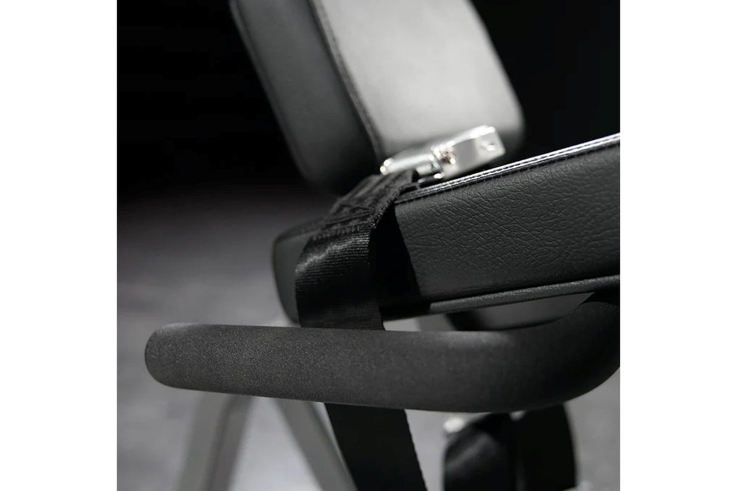 Black padded leg extension machine seat and armrest with metal adjustment lever, closeup detail