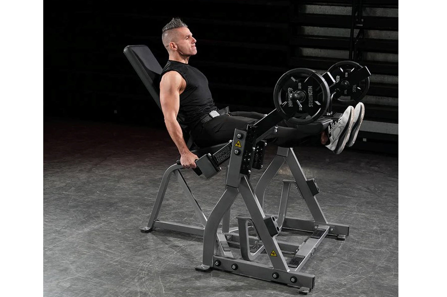 Man using black plate-loaded leg extension machine with loaded barbell in gym setting