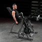 Man in black sleeveless shirt using Hammer Strength plate-loaded leg extension machine with weighted plates in gym setting