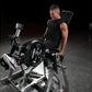 Man in black tank top using Hammer Strength plate-loaded leg extension machine with padded backrest and weight plates in gym 