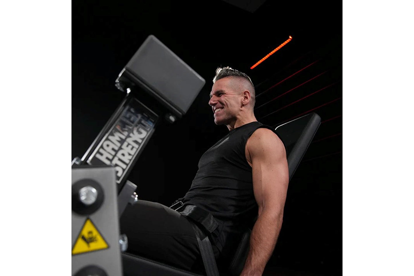 Man using Hammer Strength leg extension machine with black seat and control panel on black background
