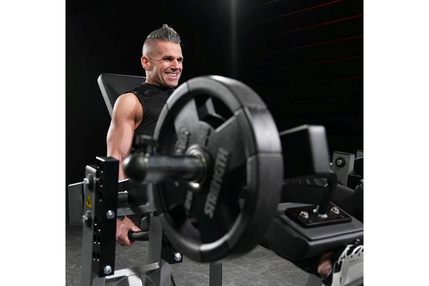 Man using black plate-loaded leg extension machine with loaded weight plates in gym setting