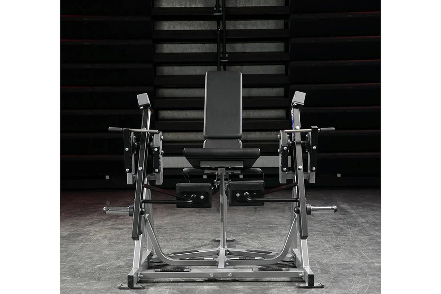 Black and silver plate-loaded leg extension machine with padded seat and dual leg extension arms, front view on gray concrete