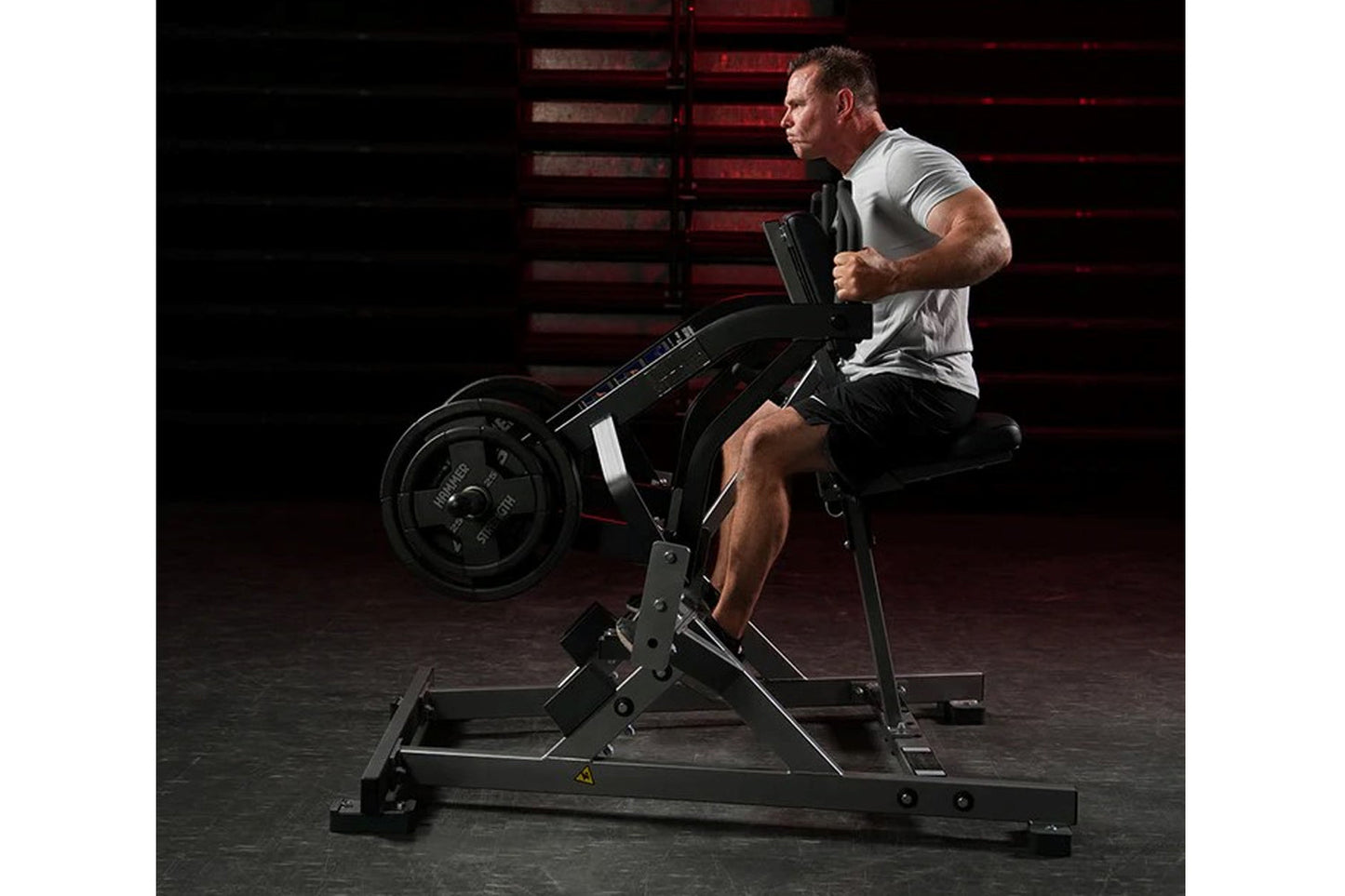 Man in gray shirt using black plate-loaded iso lateral row machine in gym setting with red stairs background