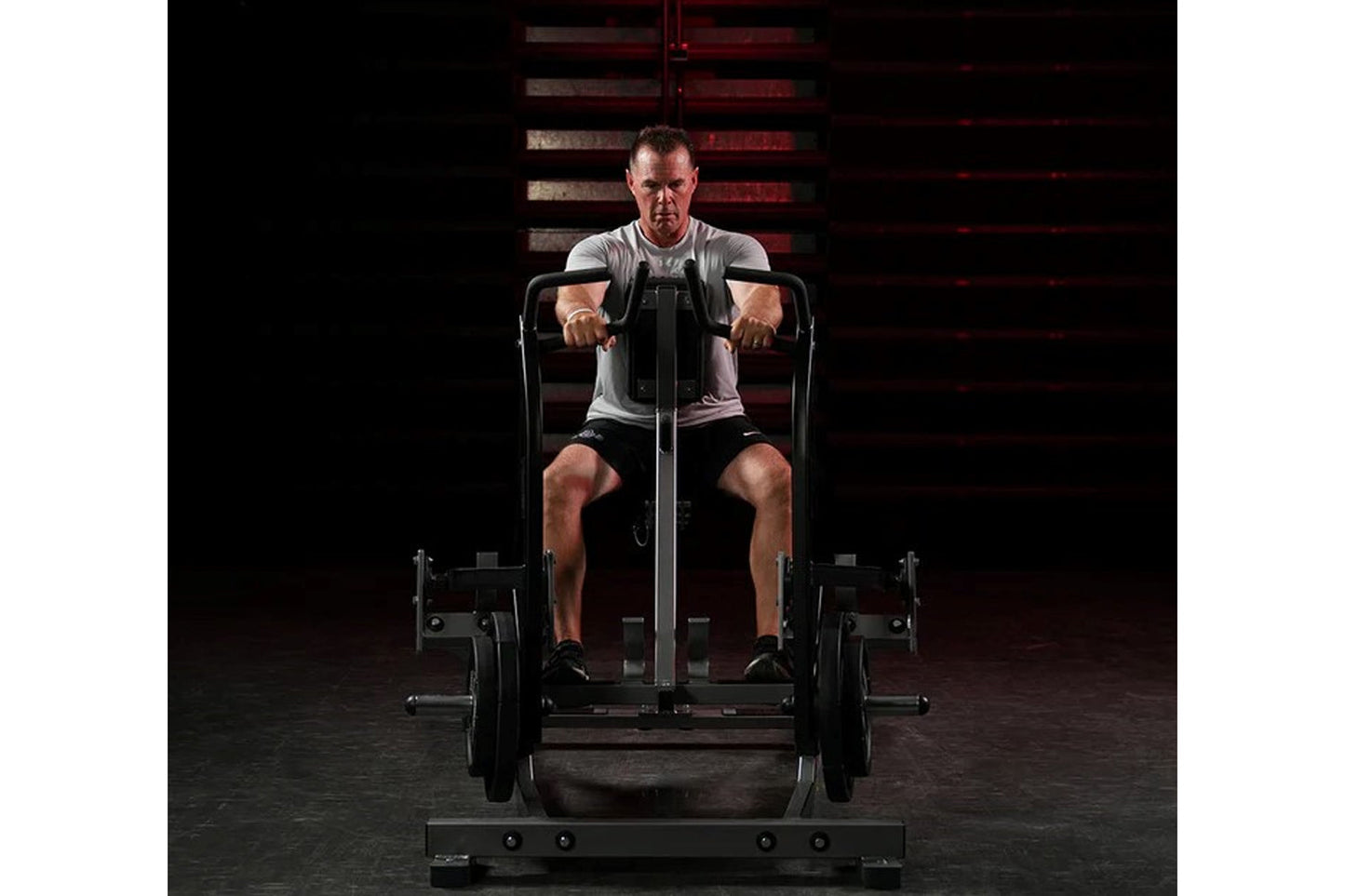 Man using black plate-loaded iso lateral row machine with gray seat, gripping handles during workout on dark gym floor
