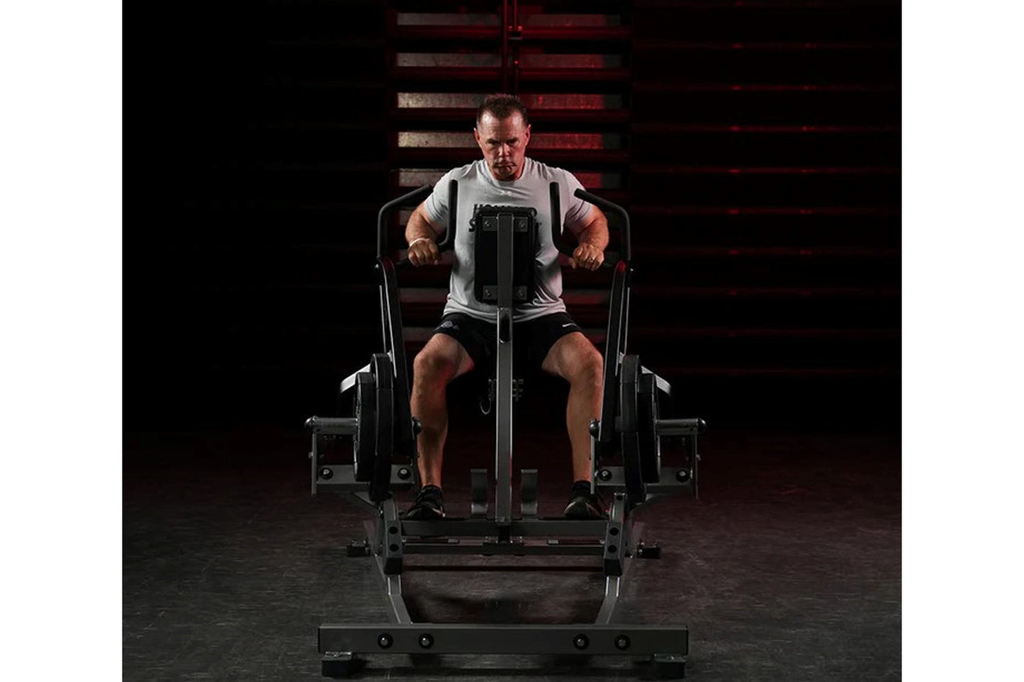 Man using black Hammer Strength plate-loaded iso lateral row machine, wearing gray t-shirt and black shorts in gym setting