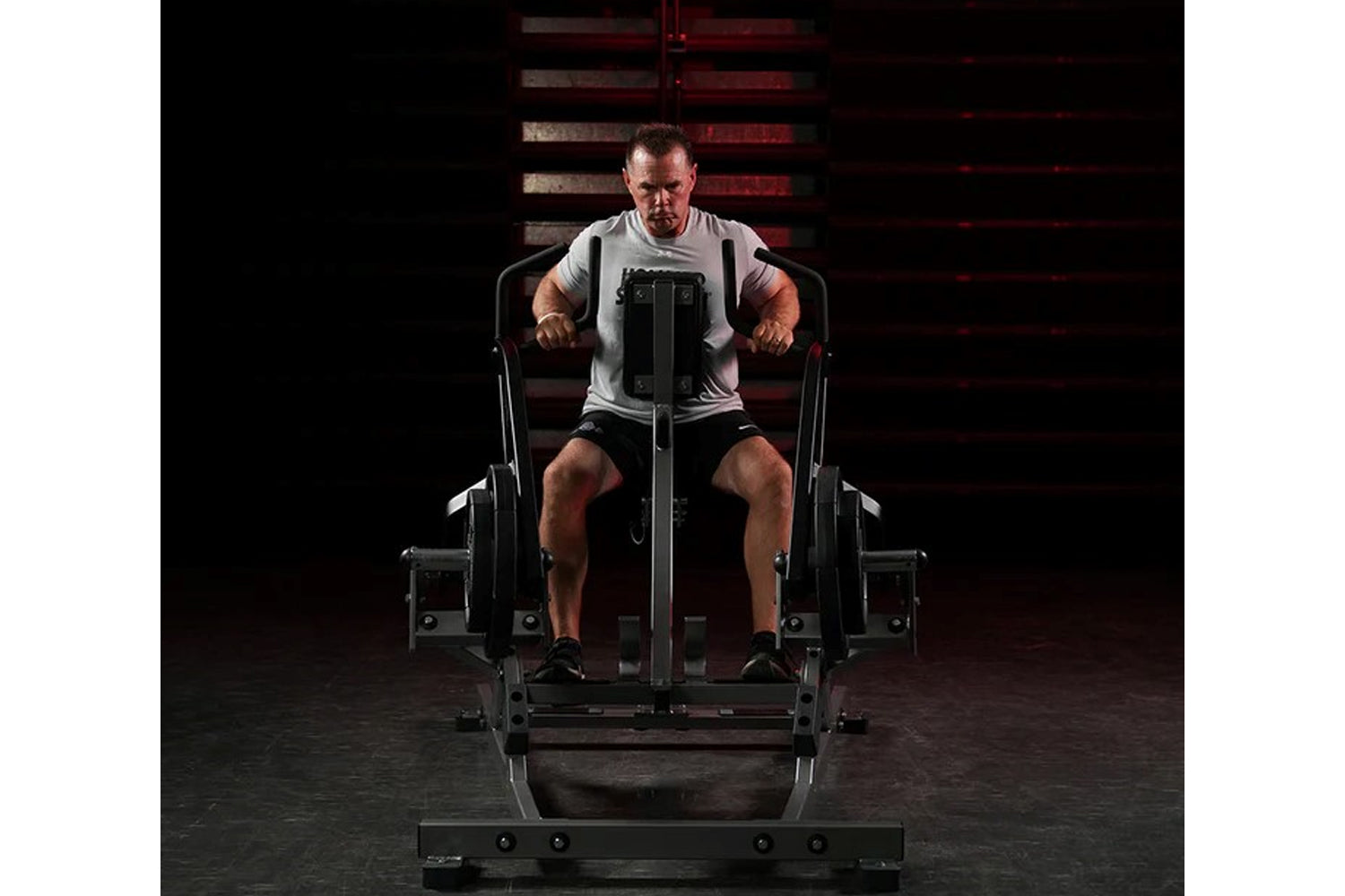 Man using black Hammer Strength plate-loaded iso lateral row machine, wearing gray t-shirt and black shorts in gym setting
