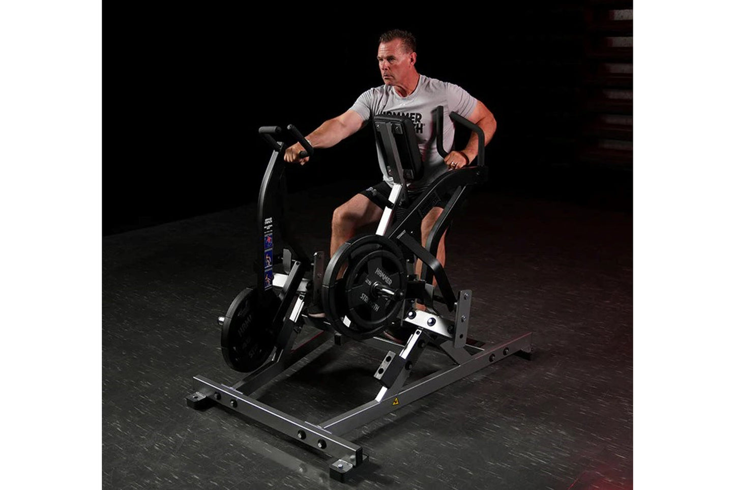 Man using black Hammer Strength plate-loaded iso lateral row machine, wearing gray t-shirt and black shorts on dark gym floor