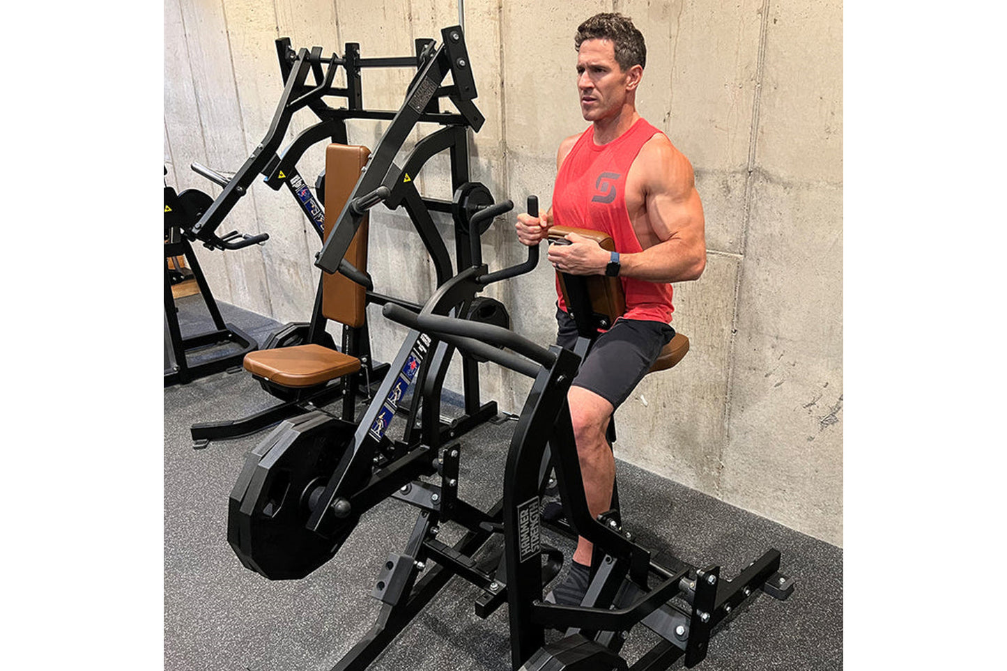 Man in red tank top using black and tan plate-loaded iso lateral row machine in gym setting