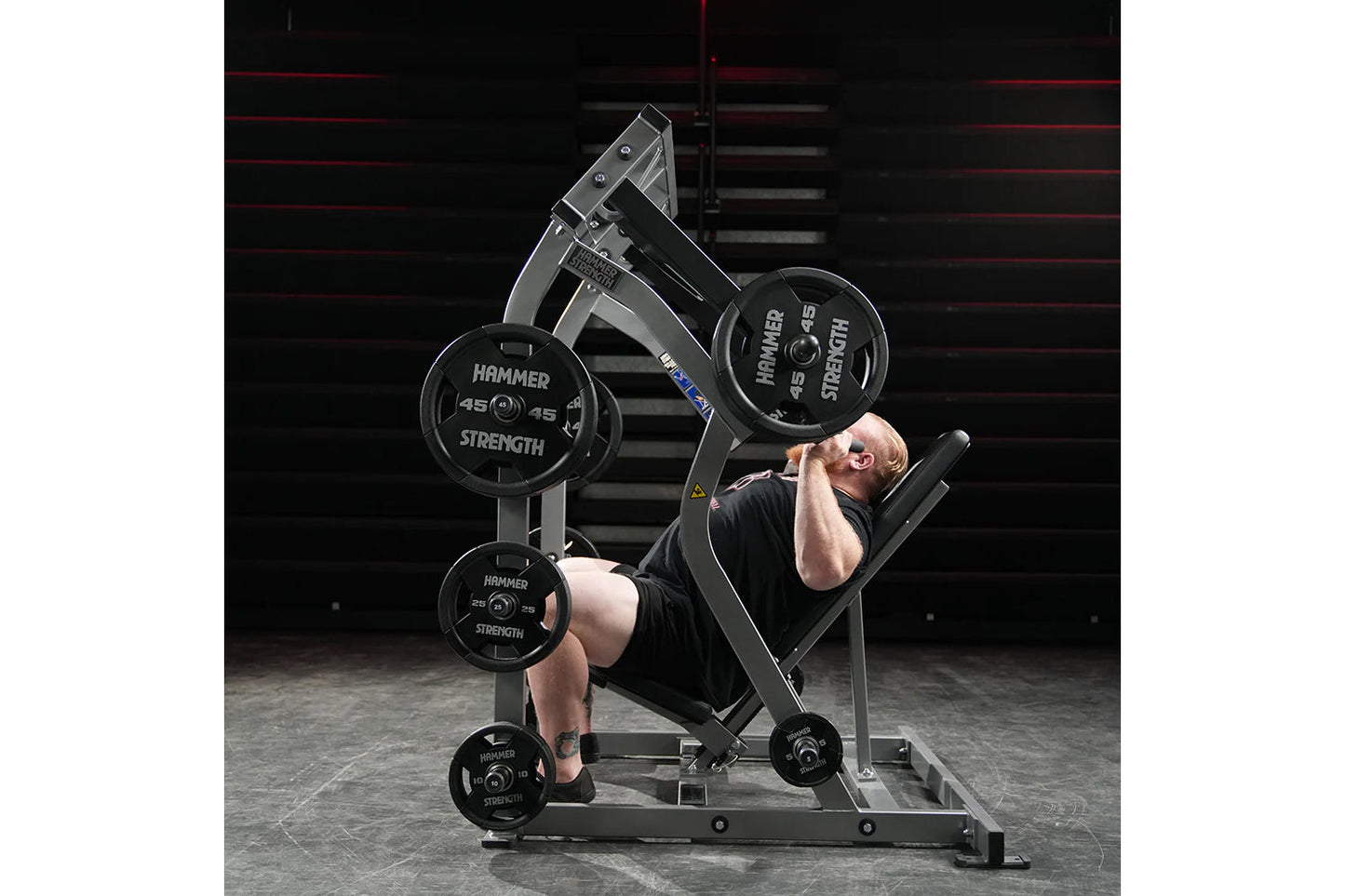 Male athlete using Hammer Strength plate-loaded shoulder press machine with black weight plates in gym setting