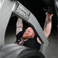 Man with red beard and chest tattoo using black Hammer Strength plate-loaded shoulder press machine in gym