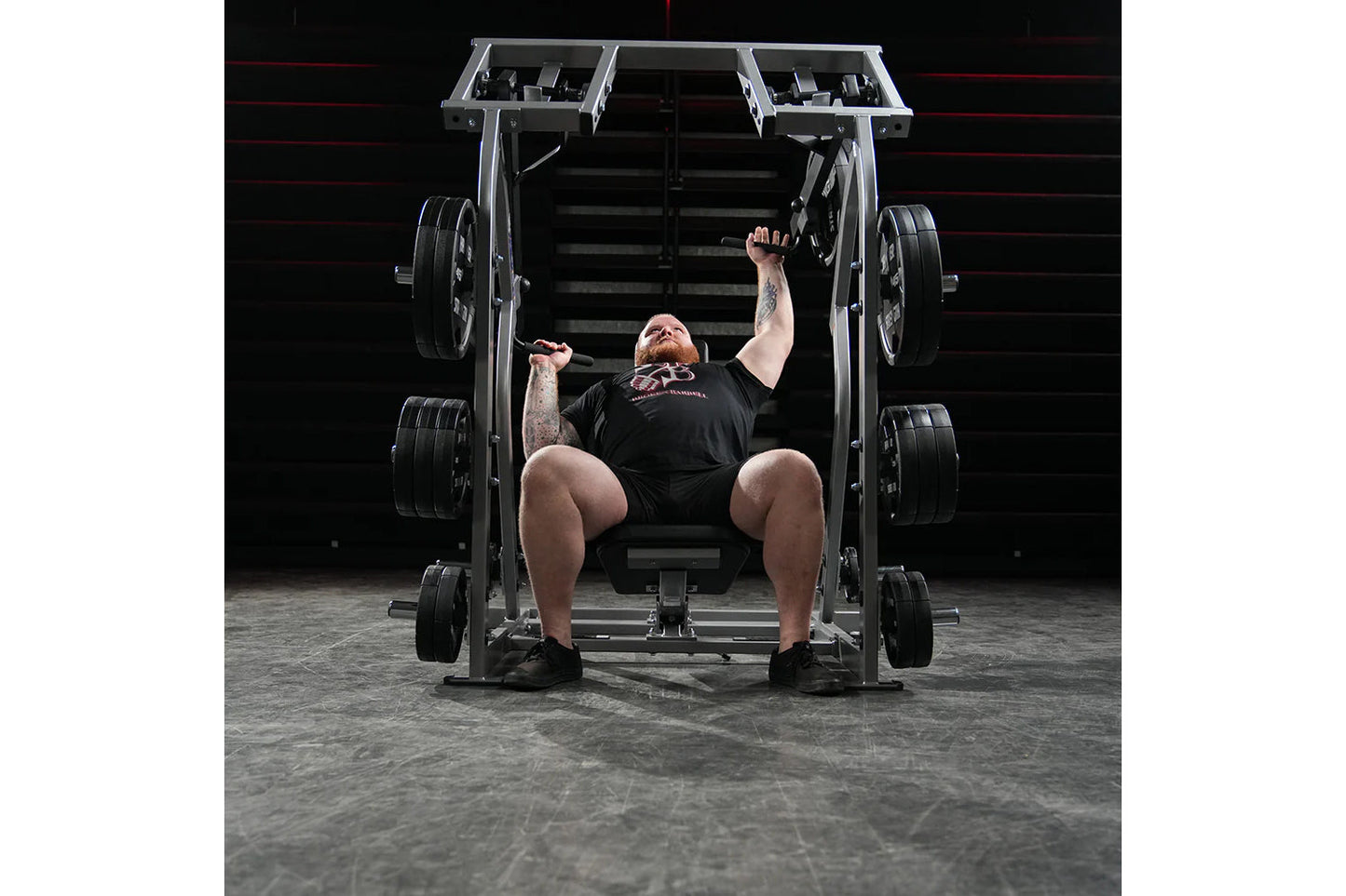 Man performing shoulder press on Hammer Strength plate-loaded machine with loaded weight plates in gym setting