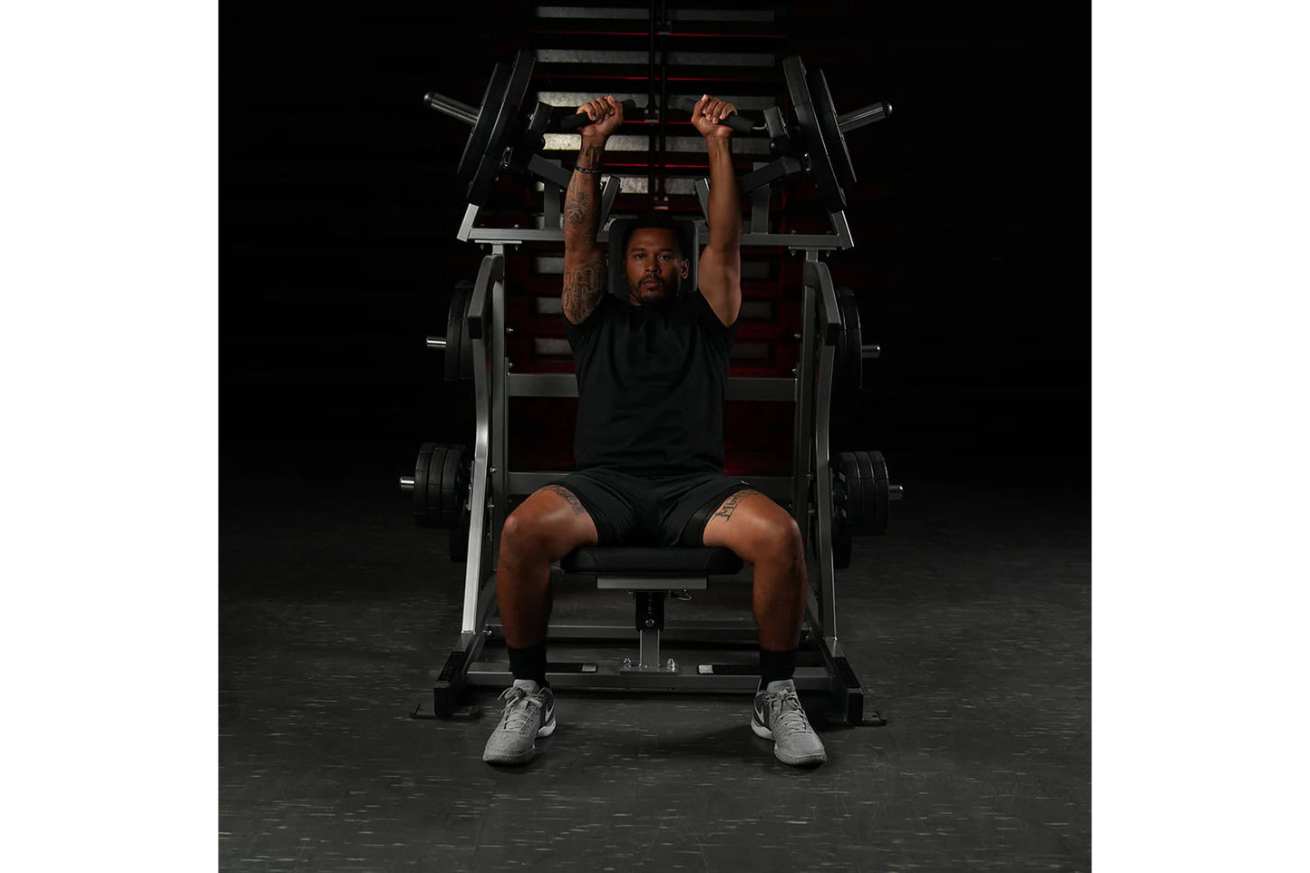 Man performing incline press on black and red Hammer Strength plate-loaded machine in gym setting