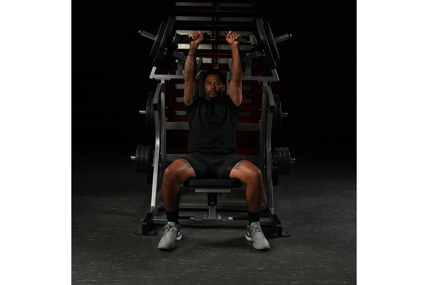 Man performing incline press on black and red Hammer Strength plate-loaded machine in gym setting