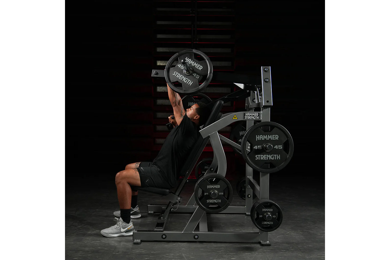 Male athlete using Hammer Strength plate-loaded iso-lateral super incline press with black weight plates, in gym setting with