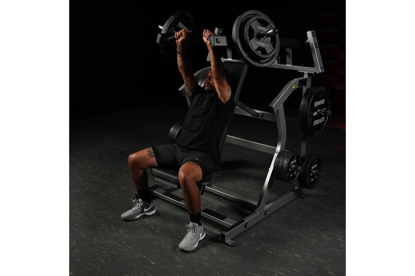 Man using black Hammer Strength plate-loaded incline press with dumbbells, demonstrating chest exercise form