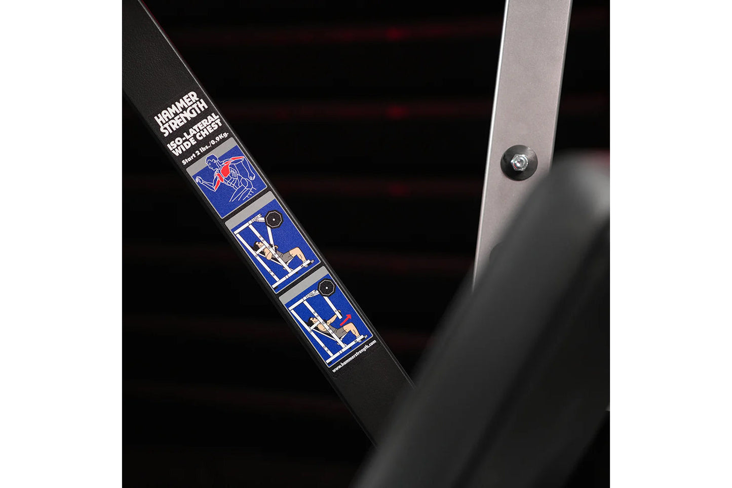Black plate-loaded chest press machine with blue and red graphic labels showing exercise instructions, detail view of side pa