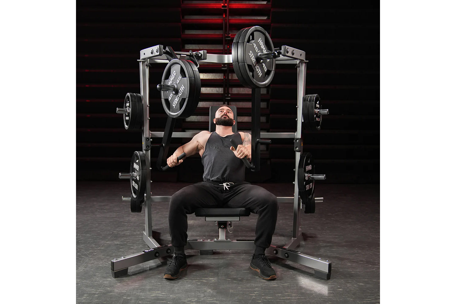 Man performing chest press on Hammer Strength plate-loaded machine with black weight plates in gym setting