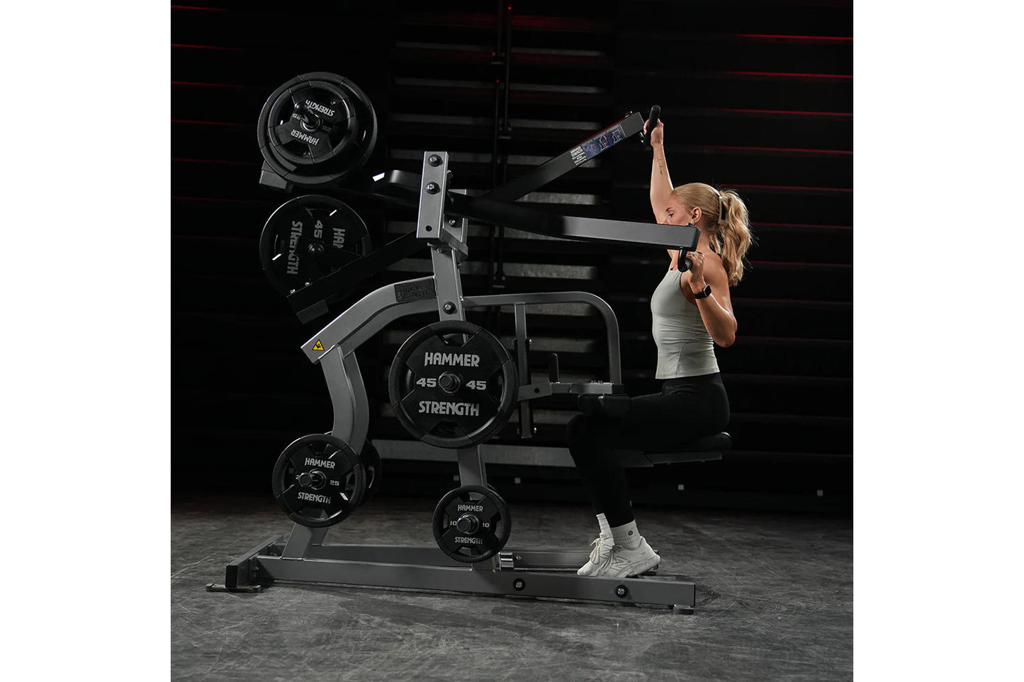 Woman using black Hammer Strength plate-loaded iso-lateral wide pulldown machine with weight plates in gym setting