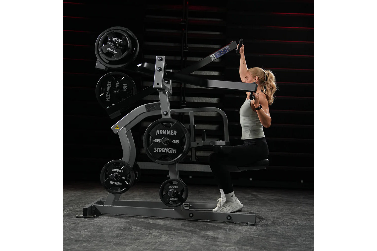 Woman using black Hammer Strength plate-loaded iso-lateral wide pulldown machine with weight plates in gym setting