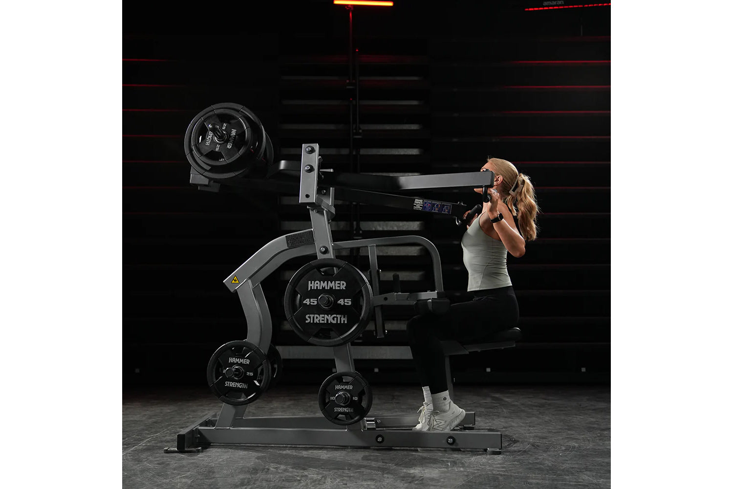 Woman using black Hammer Strength plate-loaded iso-lateral wide pulldown machine with weight plates in gym setting