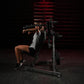 Woman using Hammer Strength plate-loaded lateral raise machine with gray tank top and black shorts in gym setting