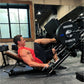 Man in red tank top using black Hammer Strength plate-loaded leg press machine with 45-pound weight plate in gym setting