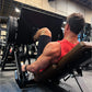 Man wearing red sleeveless tank top using black plate-loaded leg press machine in gym setting