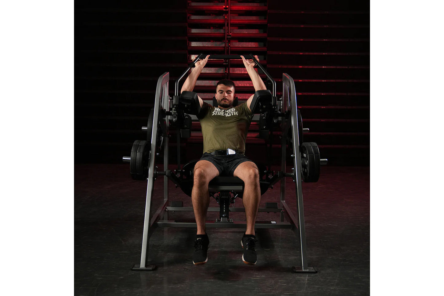 Man in olive t-shirt performing plate-loaded pullover exercise on Hammer Strength machine with red background