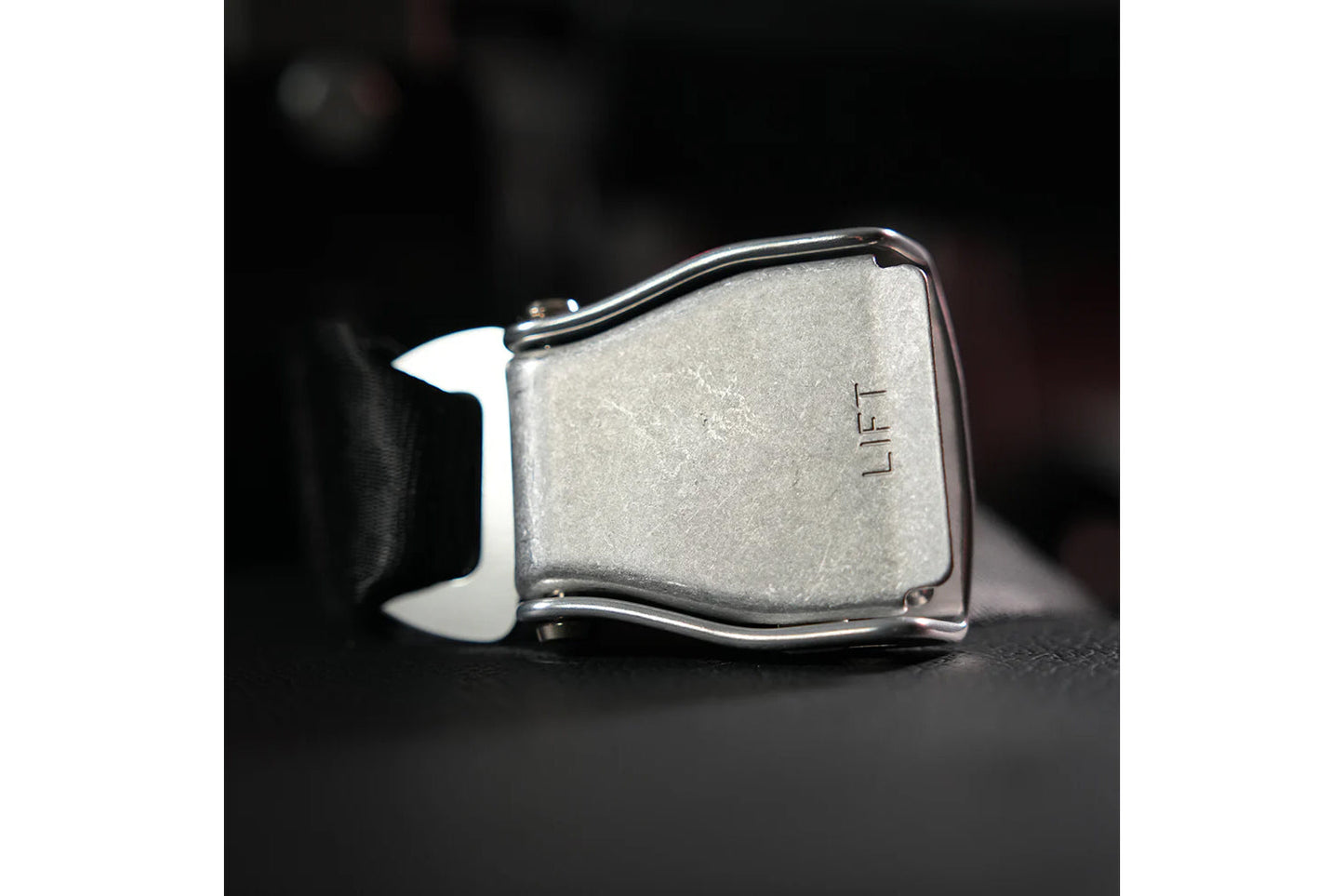 Silver metal belt buckle with "LIFT" text engraved on face, chrome hardware, on dark background